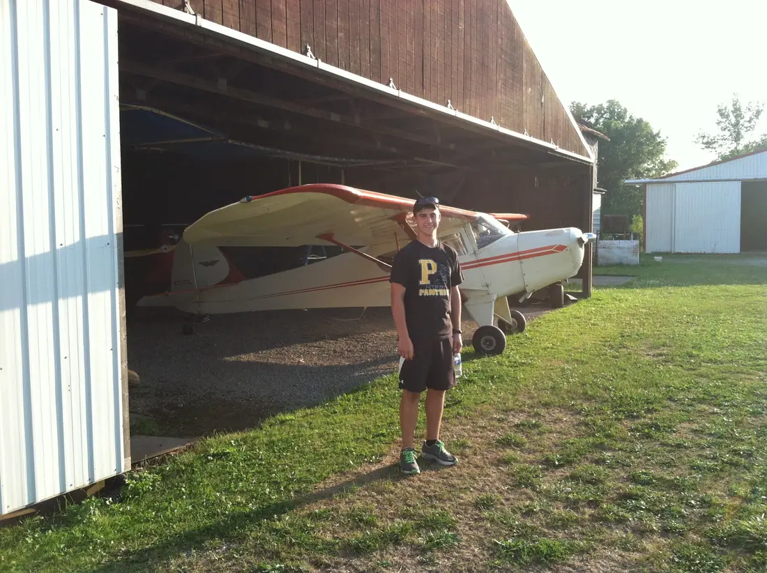 A young man standing beside two airplanes parked in an open hangar
