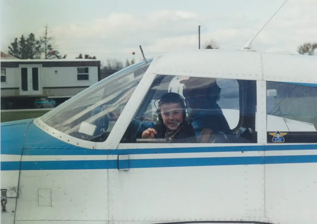 Bobby wearing a headset smiling from the cockpit of a blue and white airplane, Forrest beside him